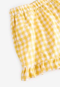 Jupe en vichy jaune et blanc avec taille élastique, ourlet volanté et broderies de petites fleurs sur le tissu. Fabriquée en coton léger.