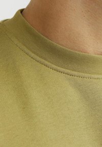 Olijfgroene katoenen t-shirt met een geribbelde ronde hals, een soepele textuur en subtiele stiksels langs de kraag.