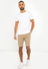 T-shirt blanche à manches courtes et shorts beiges, accompagnés de baskets blanches. Présente un design simple et une coupe régulière. Pas de motifs ni d'accents.
