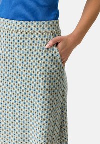 Une jupe à motifs présentant un dessin en losanges bleus et verts sur un fond clair, avec une poche visible sur le côté droit.