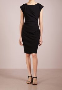 Musta muotoiltu mekko hihatin, polvipituinen malli, sileä kangas, hillitty kiertoyksityiskohta vartalon ympärillä, yhdistetty mustiin korkokenkiin.