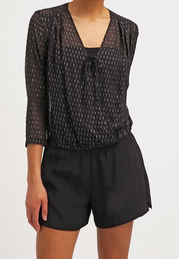 Top negro transparente con mangas 3/4, que presenta líneas verticales blancas, un escote en V y un lazo de ajuste en la parte delantera, combinado con pantalones cortos negros.