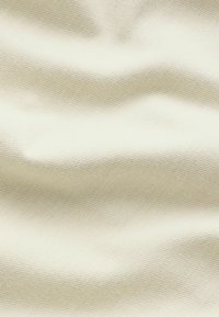 Helle cremefarbene Stoffoberfläche mit einem strukturierten, gerippten Muster. Das Material wirkt weich und fällt geschmeidig, wobei es subtile wellenartige Falten zeigt.