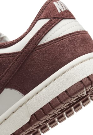 Zbliżenie na piętę bordowego zamszu i białej skóry sneakersa z fakturowaną podeszwą i widocznymi detalami szwów.