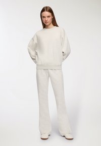 Felpa grigia chiara con taglio oversize e spalle scese, abbinata a pantaloni a palazzo coordinati. Tessuto morbido e testurizzato con un design semplice.