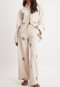 Linneblus och vida byxor set i beige med svart blommönster. Avslappnad passform, knappstängning och sidofickor i byxorna.