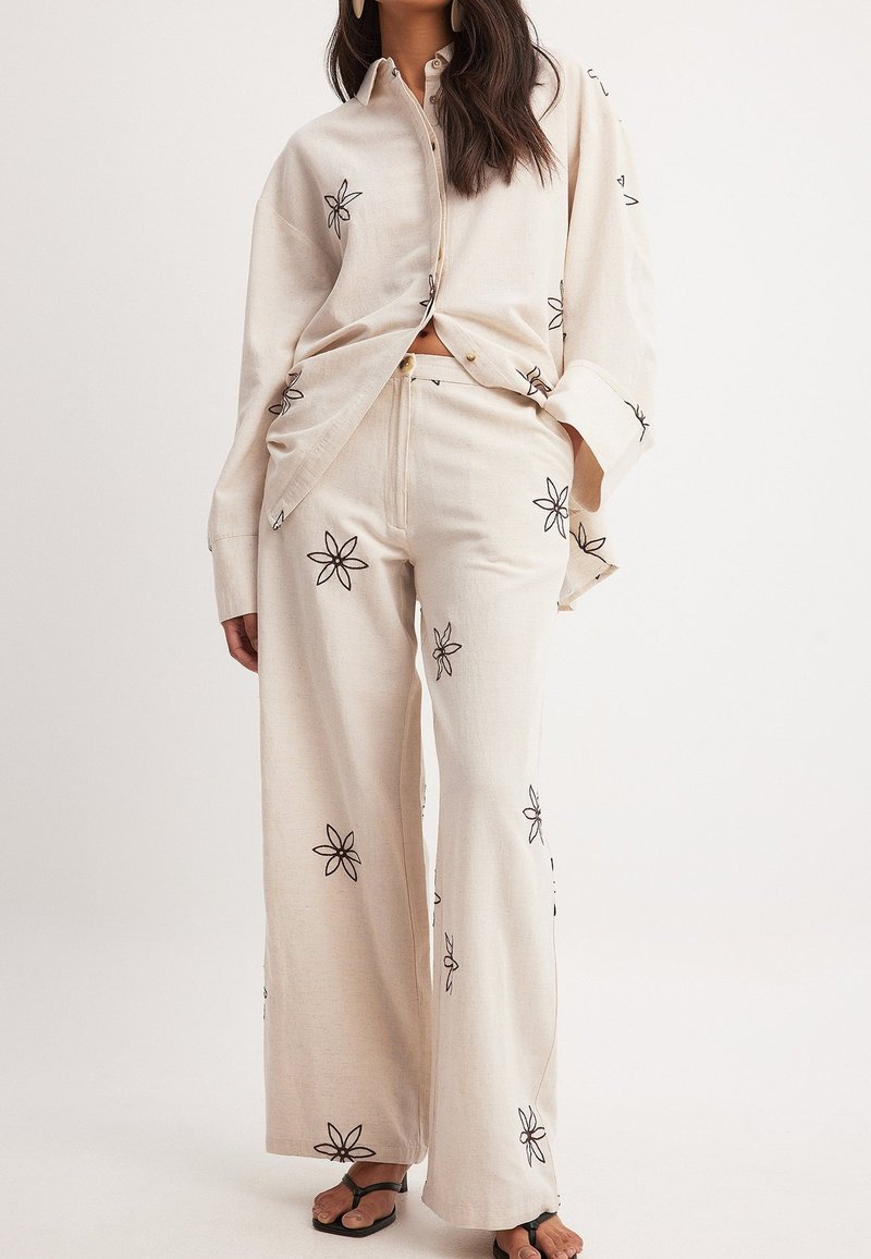 Linneblus och vida byxor set i beige med svart blommönster. Avslappnad passform, knappstängning och sidofickor i byxorna.