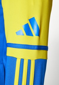 Blauwe en gele sportkledingstof met het Adidas-logo in het blauw, gestreepte textuur en een reeks verticale lijnen als accent.