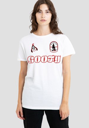 Junge Frau trägt weißes T-Shirt mit rotem "GOOFY"-Text, Goofy-Cartoon-Gesicht und schwarzem Silhouetten-Emblem auf der Brust vor einfarbigem grauem Hintergrund.