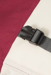 Bordowa tkanina o teksturowanym wykończeniu, w połączeniu z kremową tkaniną. Posiada czarną plastikową klamrę z szarym paskiem dla bezpiecznego zamknięcia.
