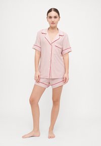 Red and white striped pajama set with short sleeves and shorts, featuring a chest pocket and red trim accents. Made of lightweight fabric.
