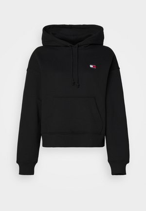 Black cropped hoodie made of soft fabric with a front pocket. Features a drawstring hood and a small logo patch on the upper left side.