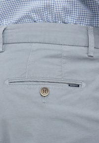 Hellblaue Baumwollhosen mit strukturiertem Finish. Verfügt über eine Gesäßtasche, die mit einem braunen Knopf mit dem eingeprägten Schriftzug "Hackett London" gesichert ist.