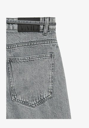Pantalon en jean gris clair montrant la poche arrière, la passants de ceinture, et une étiquette de marque noire rectangulaire près de la taille.