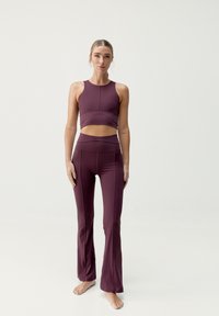 El conjunto de ropa activa burdeos incluye un top corto ajustado y leggings acampanados, fabricados con un tejido elástico de textura suave y con un diseño de costuras mínimas.