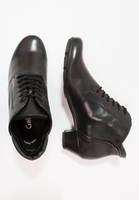 Černé kožené kotníkové boty s kulatou špičkou, šněrováním v přední části a nízkým blokovým podpatkem. Hladká textura s jemnými švy.
