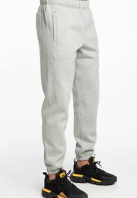 Pantalones deportivos grises de tela suave con una cintura elástica. Presenta bolsillos laterales y puños de canalé. Combinados con zapatillas deportivas negras y amarillas.