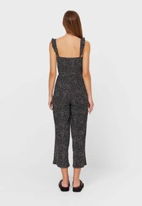 Černý overal s bílými skvrnami, nastavitelné ramínka, volánkové detaily na ramenou, vypasovaný korzet a zkrácený široký střih nohavic.