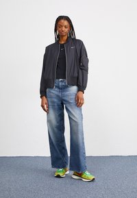 Svart bomberjacka med dragkedja, åtsittande ärmslut och sidoficka. Svart t-shirt, ljusblå vida jeans och färgglada sneakers med gröna och gula detaljer.