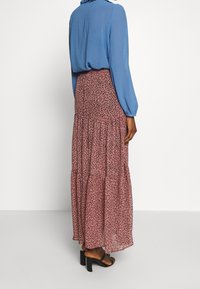 Blomstret maxikjole i pink med sorte leopardpletter, lagdelt design, letvægtsstof, parret med en blå skjorte med lange ærmer og sorte blokhælede sandaler.