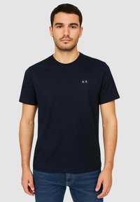 Maglietta in cotone blu navy con collo rotondo e maniche corte, caratterizzata da un piccolo logo bianco sulla parte sinistra del petto. Tessuto liscio.