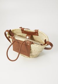 Borsa a spalla intrecciata in paglia con inserti in pelle marrone, manici intrecciati, chiusura con zip e un'etichetta in pelle timbrata. Forma rotonda, design leggero.