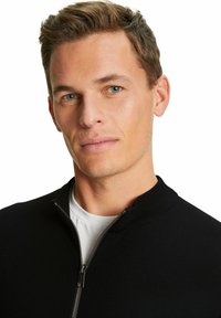 Schwarzer Reißverschluss-Pullover mit hohem Kragen und gerippter Textur, über einem weißen Hemd getragen, mit silbernem Reißverschluss und minimalistischer Gestaltung.