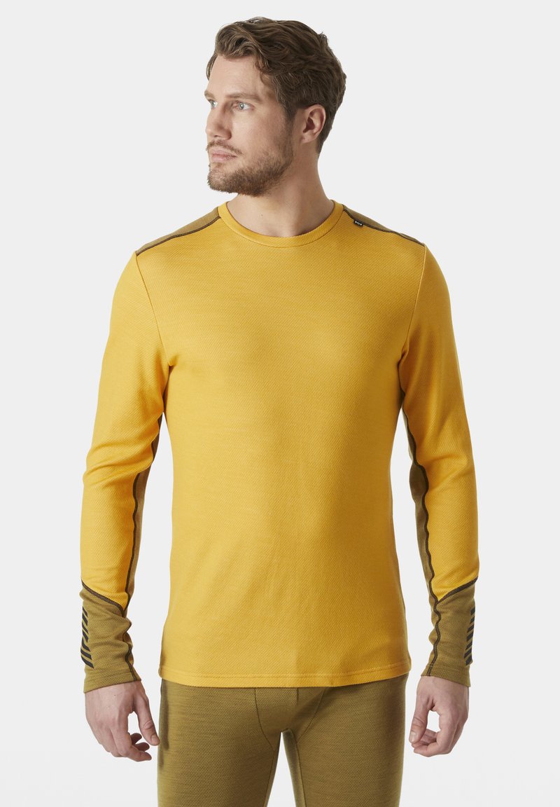 Žlutá dlouhá košile s texturovanou tkaninou a kontrastními rukávy, které mají hnědý akcent a pruhované detaily blízko zápěstí.