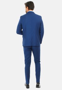 Abito blu in tessuto, con un design slim fit. I pantaloni si restringono alla caviglia, mentre la giacca ha un taglio dritto e accenti minimalisti.