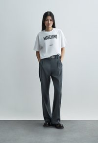 Fehér pamut póló fekete "MOSCHINO Milano" felirattal, szürke, magas derekú nadrággal és fekete lábbelivel párosítva. Sima anyag, laza szabás.