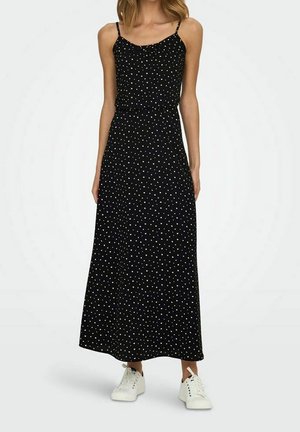 Zwarte maxi-jurk met spaghettibandjes, met een wit polkadotpatroon, gemaakt van een zachte stof. Gecombineerd met witte sneakers.