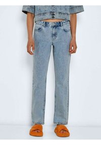 Jeans de denim azul claro com corte reto, cinco bolsos e um leve efeito desbotado. Combinados com sandálias slip-on texturizadas laranja.