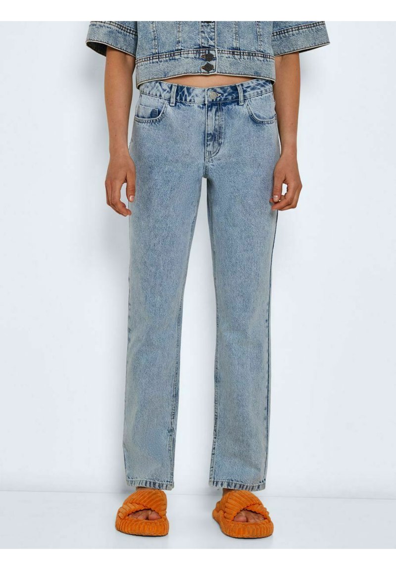 Jeans de denim azul claro com corte reto, cinco bolsos e um leve efeito desbotado. Combinados com sandálias slip-on texturizadas laranja.