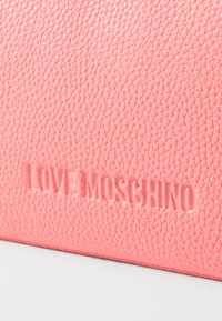 Rožinė tekstūruota odinė piniginė, kurioje iškeltos "LOVE MOSCHINO" prekės ženklo raidės, pasižyminti lygiu paviršiumi su lengvu blizgesiu.