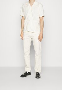 Korte mouwen, geruit overhemd in licht crème met twee voorzakken, gecombineerd met slim-fit crème broek en zwarte instappers.