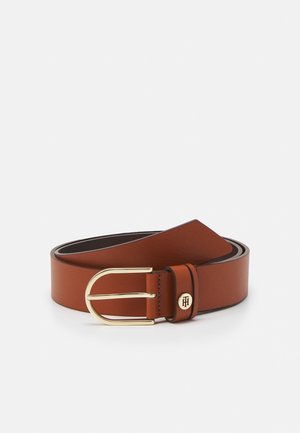 Ceinture en cuir marron roulée avec une boucle rectangulaire arrondie dorée et un petit logo circulaire sur la boucle de la ceinture.