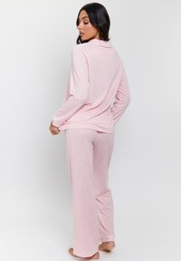 Roze geribbelde pyjamaset met een lange mouw top met kraag en bijpassende recht afgesneden broek met een relaxte pasvorm. Zacht, gestructureerd materiaal.
