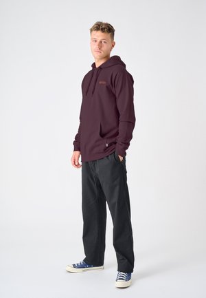 Maroon hoodie with a front pocket and drawstring hood, featuring "Dream" in contrasting orange text. Paired with black pants and blue sneakers.
