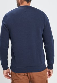 Sudadera azul marino confeccionada en mezcla de algodón, con cuello redondo, mangas largas y dobladillo acanalado. Textura suave con un detalle mínimo.