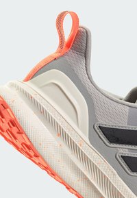 Grå atletiske sko med orange accenter, struktureret overdel, tynde sorte striber og sål med hvide sprøjt. Har en løkke ved hælen.