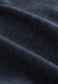 Ingrandimento di un morbido tessuto di lana blu scuro con una texture a maglia fine e pieghe sottili che creano ombre e riflessi.