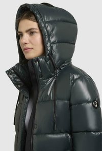 Puffet mørkegrøn hættejakke med en blank finish, der har en høj krave, snoretræk, lynlås lukning og logo patch på ærmet.