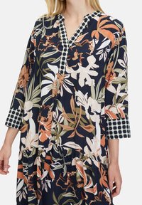 Námořnické šaty s květinovými vzory v oranžové, bílé a zelené barvě. Obsahují výstřih do V s kontrastním lemováním a rukávy o délce 3/4 s puntíkovaným okrajem.