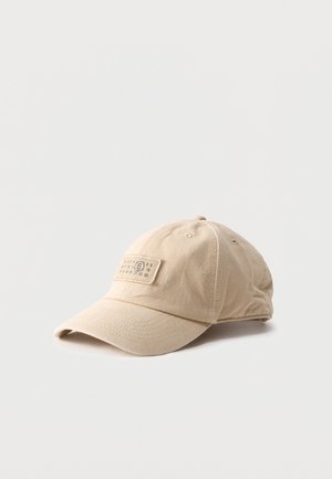 Beżowa bawełniana czapka bejsbolowa z naszywką z przeszyciami przedstawiającą serię liczb na przednim panelu, umieszczona na jednolitym jasnym tle.