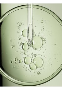 Helder glazen schaal met groene vloeistof en luchtbelletjes. Een pipet is gedeeltelijk ondergedompeld en heeft een gladde, langgerekte vorm.