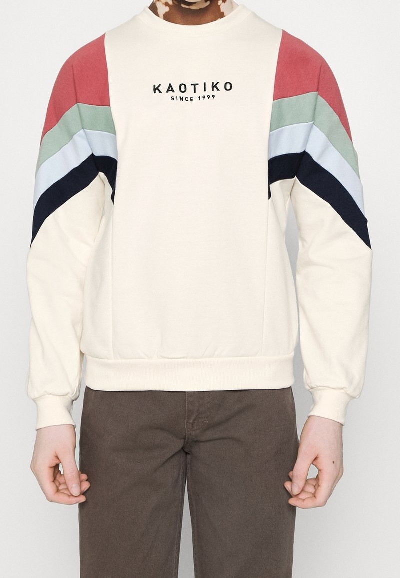 Felpa crema con maniche a blocchi di colore rosso, verde, blu e blu navy. Presenta un collo rotondo e polsini a costine. Logo del marchio presente.