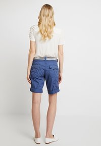 Pantaloncini cargo blu con risvolti arrotolati, dotati di tasche frontali e posteriori. Abbinati a un top a maniche corte di colore chiaro e scarpe basse.