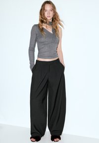 Top grigio monospalla abbinato a pantaloni neri larghi; entrambi con texture lisce. Il top presenta un design con ritagli; i pantaloni sono a vita alta.