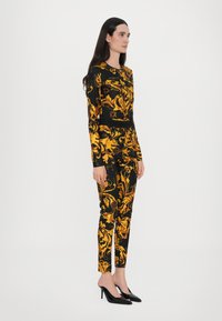 Black outfit with gold floral pattern; long-sleeve top and tapered pants; smooth texture; worn with black high-heel shoes.
