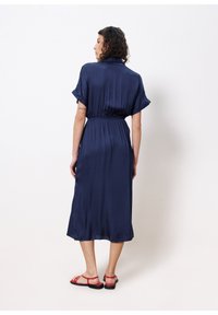 Navyblaue, knielange Kleider mit kurzen, umgeschlagenen Ärmeln, elastischem Bund und glatter Textur. Kombiniert mit roten Sandalen mit verstellbaren Riemen.